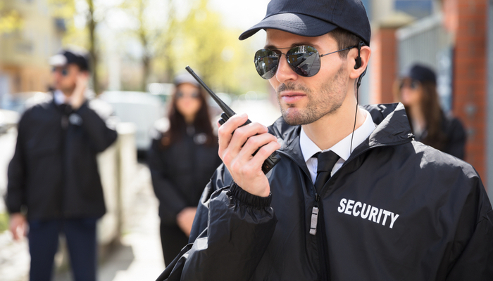 Security guard with black jacket sunglasses and cap on duty talking on walkie talkie radio