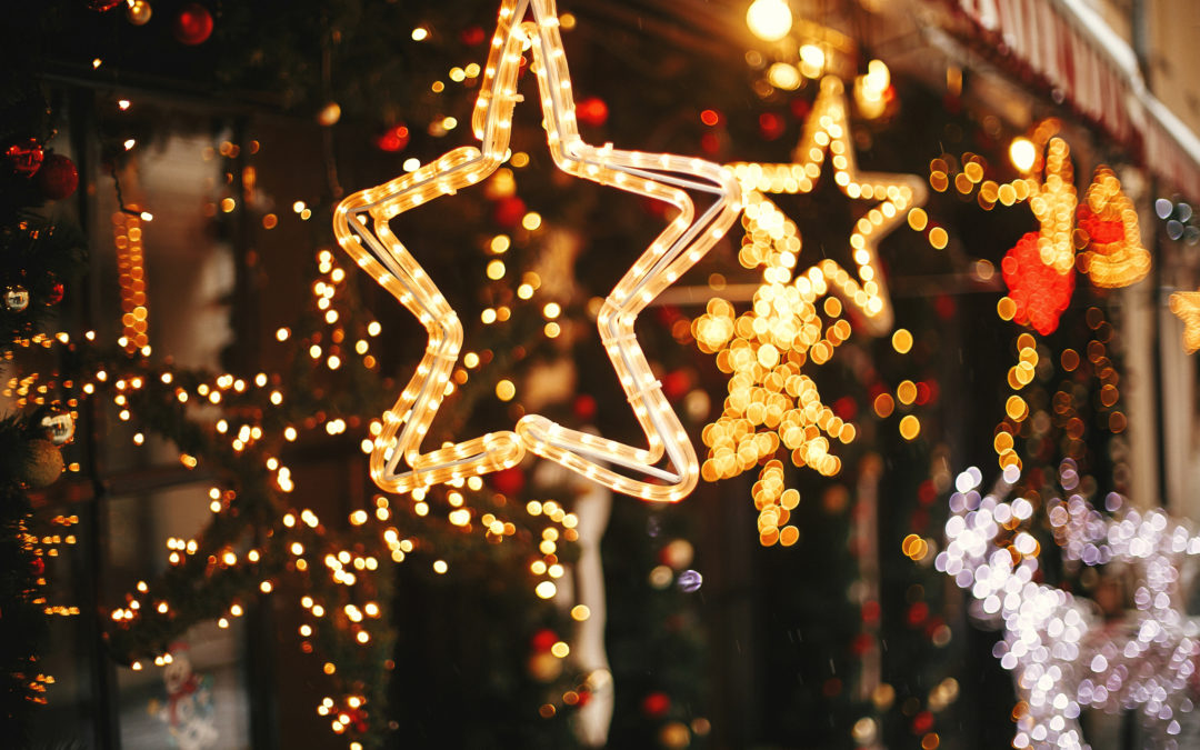 Stylish christmas golden star illumination and fir branches with red and gold baubles, golden lights bokeh on front of building at holiday market in city street. Christmas street decor