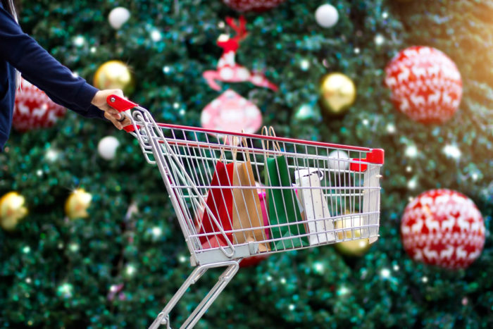 Christmas shopping woman shopper with bags in shopping cart on holidays ornament and christmas tree on street background